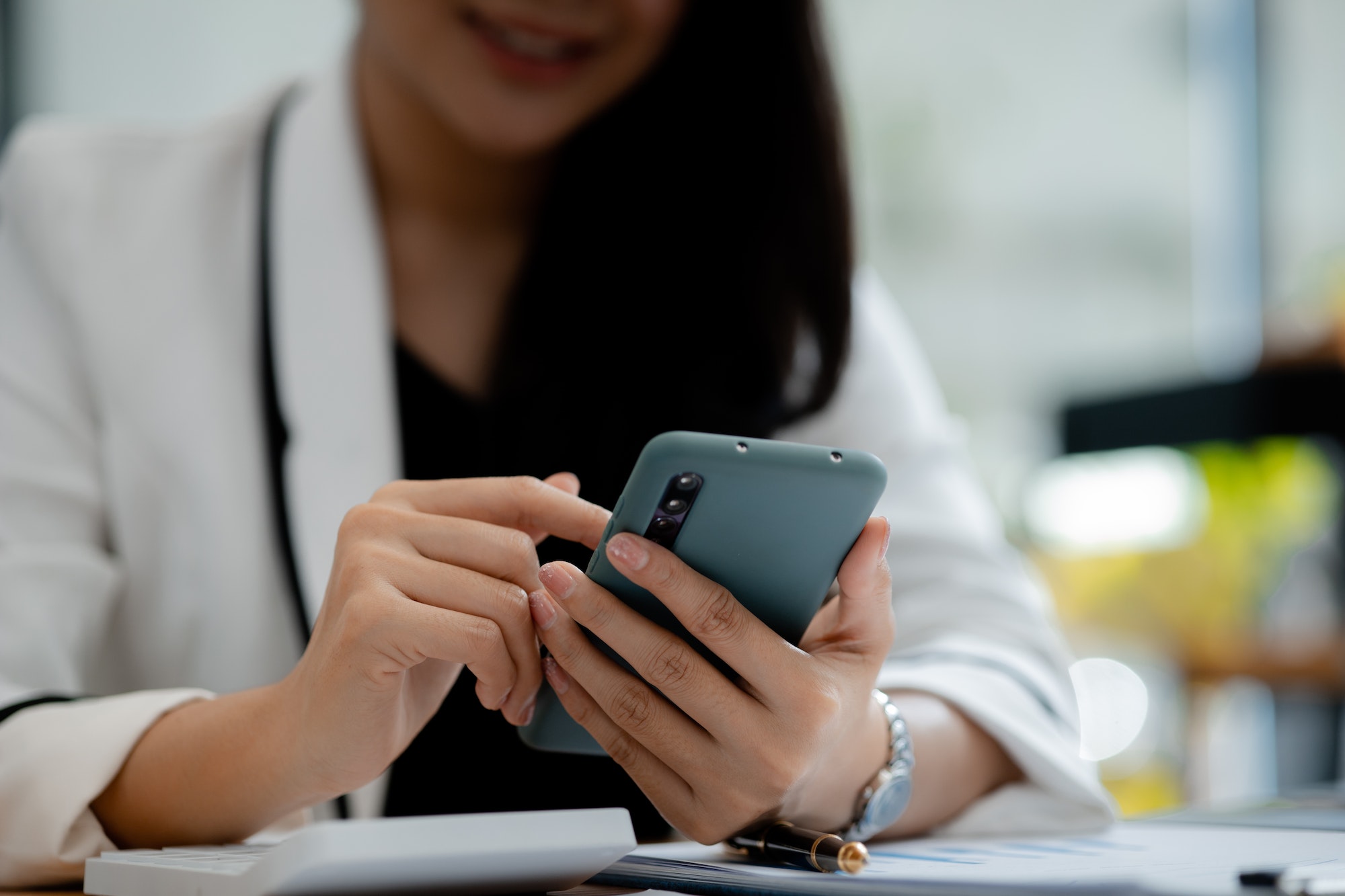 Beautiful Asian woman playing mobile phone in her break from work, she is a marketing manager of a s